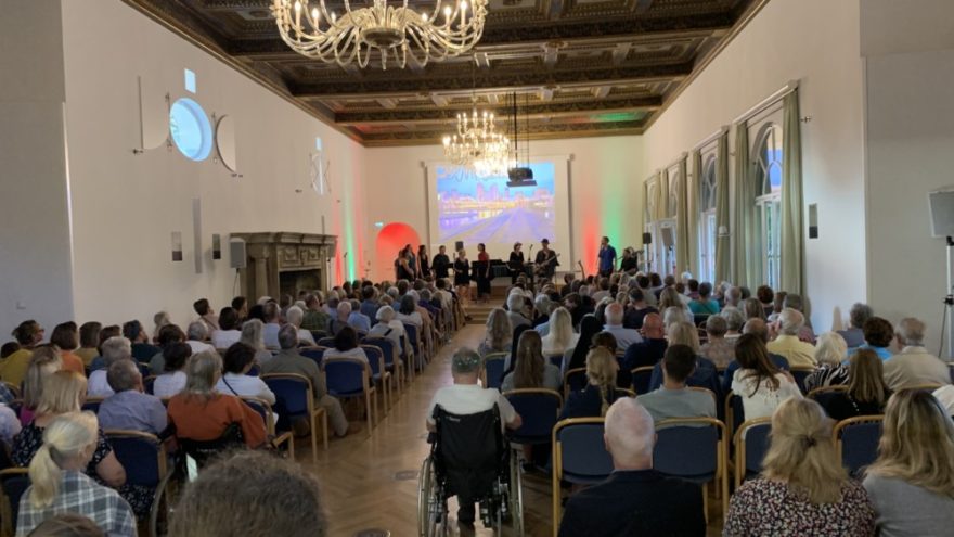 Blue Notes Sommerkonzert 2 240724 BlueNotesSommerkonzert RN01 - Wenn die Blue Notes unter der Leitung von Waltraud Brod im Musiksaal der Evangelischen Akademie Tutzing ihr Sommerkonzert spielen, passt keine Maus mehr in den Raum. Am Mittwoch, den 24. Juli 2024 war es wieder soweit. Bis zum letzten Platz gefüllt und noch draußen vor den Fenstern lauschten die Gäste den Liedern, die von Frieden und Freiheit handelten und auch die Herzen berührten. Diesmal hatte der Chor für einen Gastauftritt die Band „Angels’ Share“ eingeladen, die nach der Pause vier ihrer selbstgeschriebenen Lieder spielten. Unterstützt wurden die Sänger der Band von einem kleinen Hintergrundchor aus den Blue Notes. Der Chor freute sich über die Resonanz und ließ den erfolgreichen Abend an diesem lauen Sommerabend im schönen Park der Akademie ausklingen.