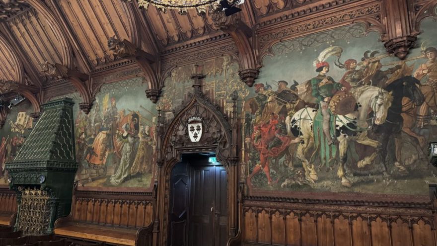 2025 10 18 KDFB Landshut RN06 - Im Oktober 2025 fuhr eine Gruppe des Frauenbund Tutzing nach Landshut. Die Stadtführerin Jutta Beer vom Tourismusbüro der Stadt empfing uns sehr herzlich. Wir gingen zunächst in den Rathaussaal, der mit Wandmalereien der Landshuter Hochzeit ausgestattet und bereits 140 Jahre alt ist. Hier wurden damals wichtige Entscheidungen getroffen. Heute finden hier Konzerte und Empfänge statt. Wir erfuhren allerlei nette Geschichten und Bräuche der damaligen Zeit, so zum Beispiel, dass die Hochzeit vor 500 Jahren die teuerste und größte mit 10.000 Gästen war, eine Woche gedauert hat und umgerechnet 20 Mio Euro gekostet hat. Die Stadt hatte Geld, da hier die Steuer und der Zoll erfunden wurden. Sie erzählte uns, dass die polnische Braut mit 18 Jahren schon zu alt war, aber der Herzog auch erst 20 war und so es ein guter Start für die Ehe war. Am Hochzeitstag gab es ein 35-Gänge Menü und wir stellten uns vor, wie man so viel Essen kann und wie man sich dabei wohl fühlt.